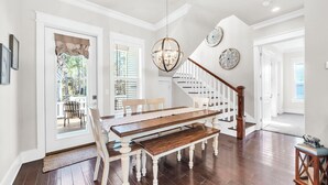 Un comedor con mesa y banco de madera, una araña y una escalera con barandillas blancas.