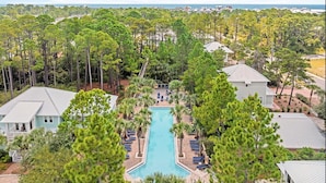 Un resort con piscina central rodeada de sillas de descanso, y densos pinos, con vista al océano.