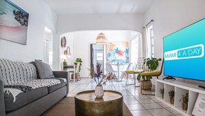 Un salón moderno con un sofá gris, una mesa de centro y un televisor mostrando 'MIAMI 4 A DAY'.