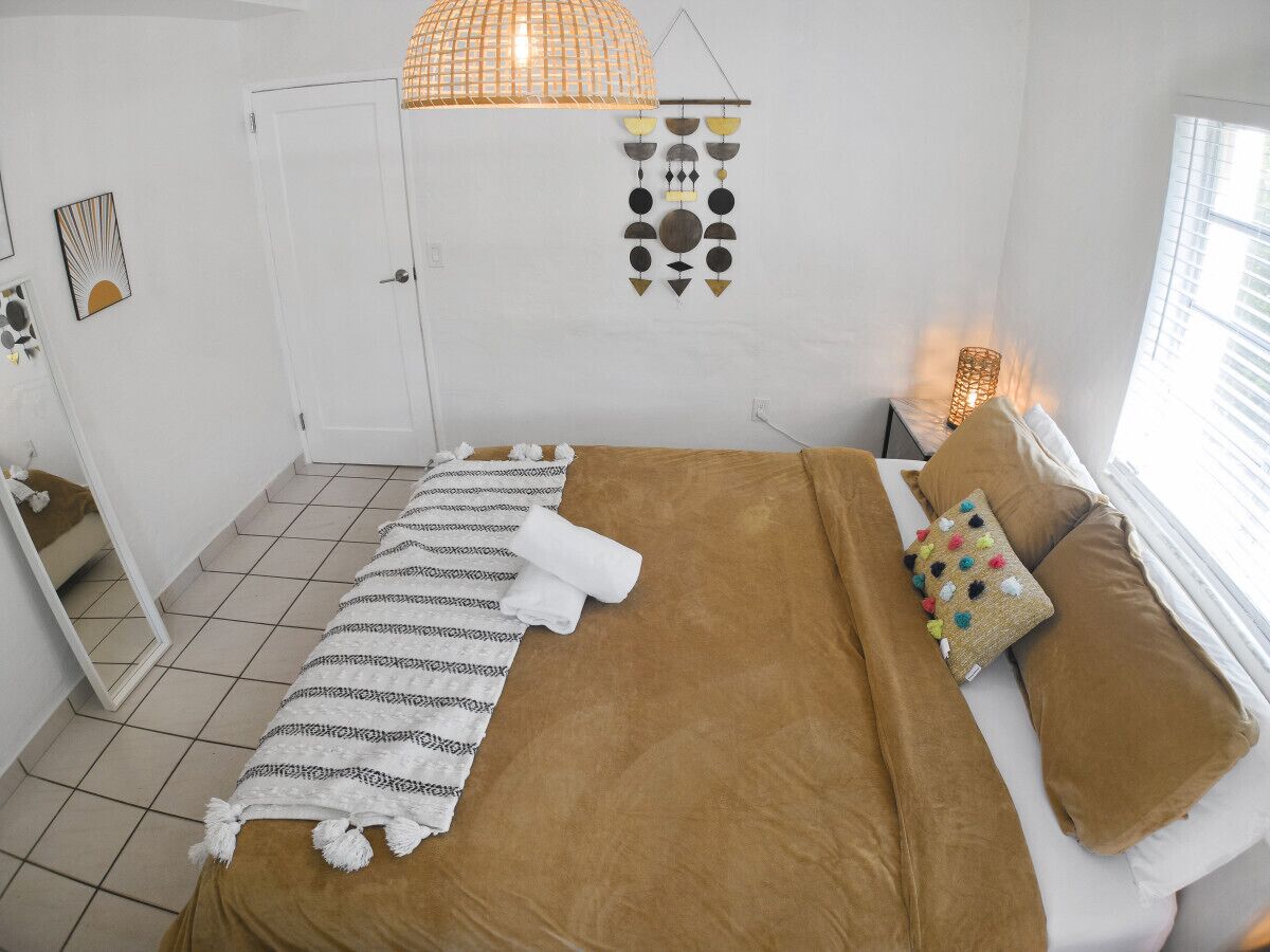 A bedroom with a bed, pillows, a hanging light fixture, and wall art.