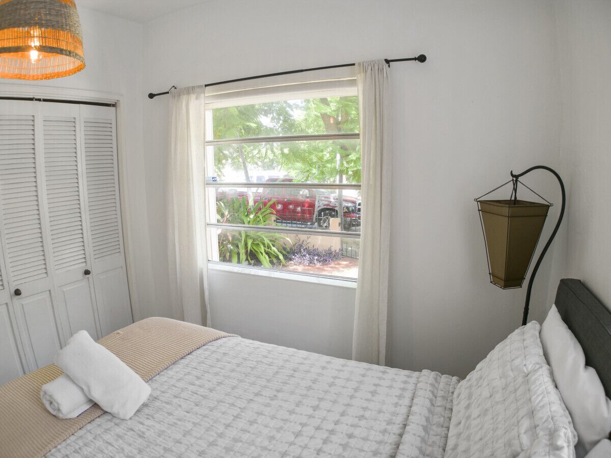 A bedroom with a bed, a window with curtains, a hanging lamp, and a view of the outside.