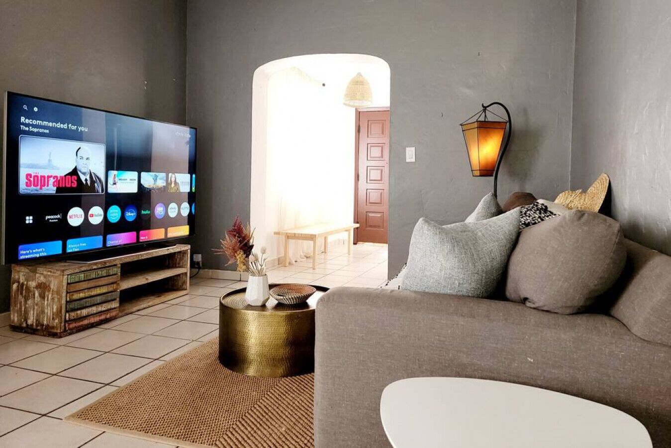 Un salon équipé d’un téléviseur à écran plat affichant l’interface d’un service de diffusion en continu, d’un canapé, d’une table basse agrémentée d’objets décoratifs et d’une lampe fixée au mur.
