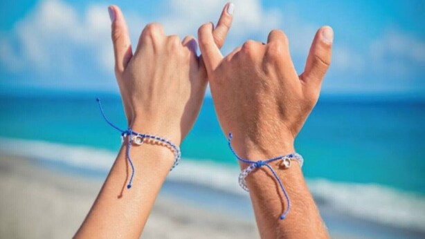 Dos manos con pulseras sobre un fondo de playa.