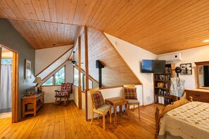 A cozy attic bedroom with wooden floors, a sloped ceiling, a bed, a TV, a bookshelf, and a window. - River | Hot Tub | Firepit & BBQ | Dogs | Deck (Leavenworth)
