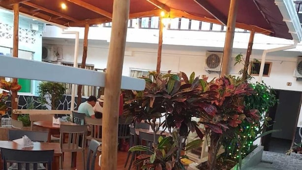 Un área de comedor al aire libre con mesas y sillas de madera, rodeada de macetas con diversas plantas.