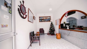 Un área de recepción con una silla de madera, un árbol de Navidad, un reloj y un cuadro en la pared.