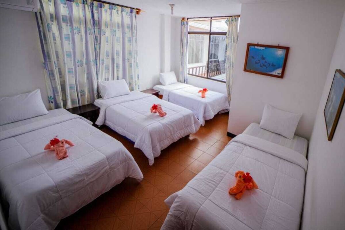 A hotel room with three beds, a window with curtains, a wall-mounted TV, and a framed picture.