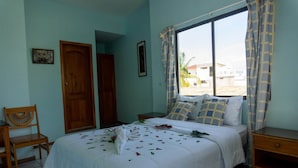 Un dormitorio con cama, una silla, un armario de madera, ventana con cortinas y vistas al exterior.