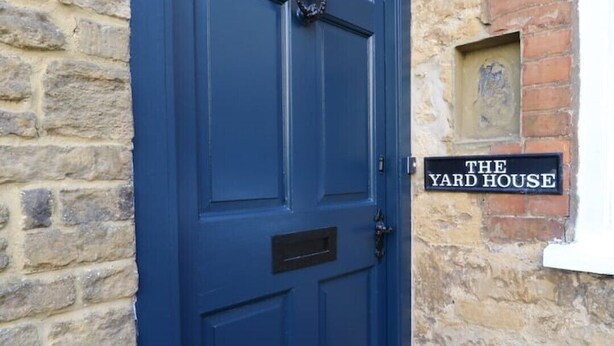 Una porta blau fosc amb una placa negra que diu “THE YARD HOUSE”.