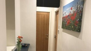 Un passadís amb una porta de fusta, una taula consola negra amb un ram de flors i un quadre a la paret.