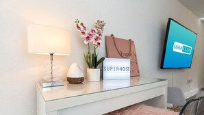 A modern room with a glass desk, a lamp, a potted orchid, a sign reading "SUPERHOST," and a TV displaying "MIAMI 4 A DAY." - Lovely Apartment Near Brickell 1 (Miami)