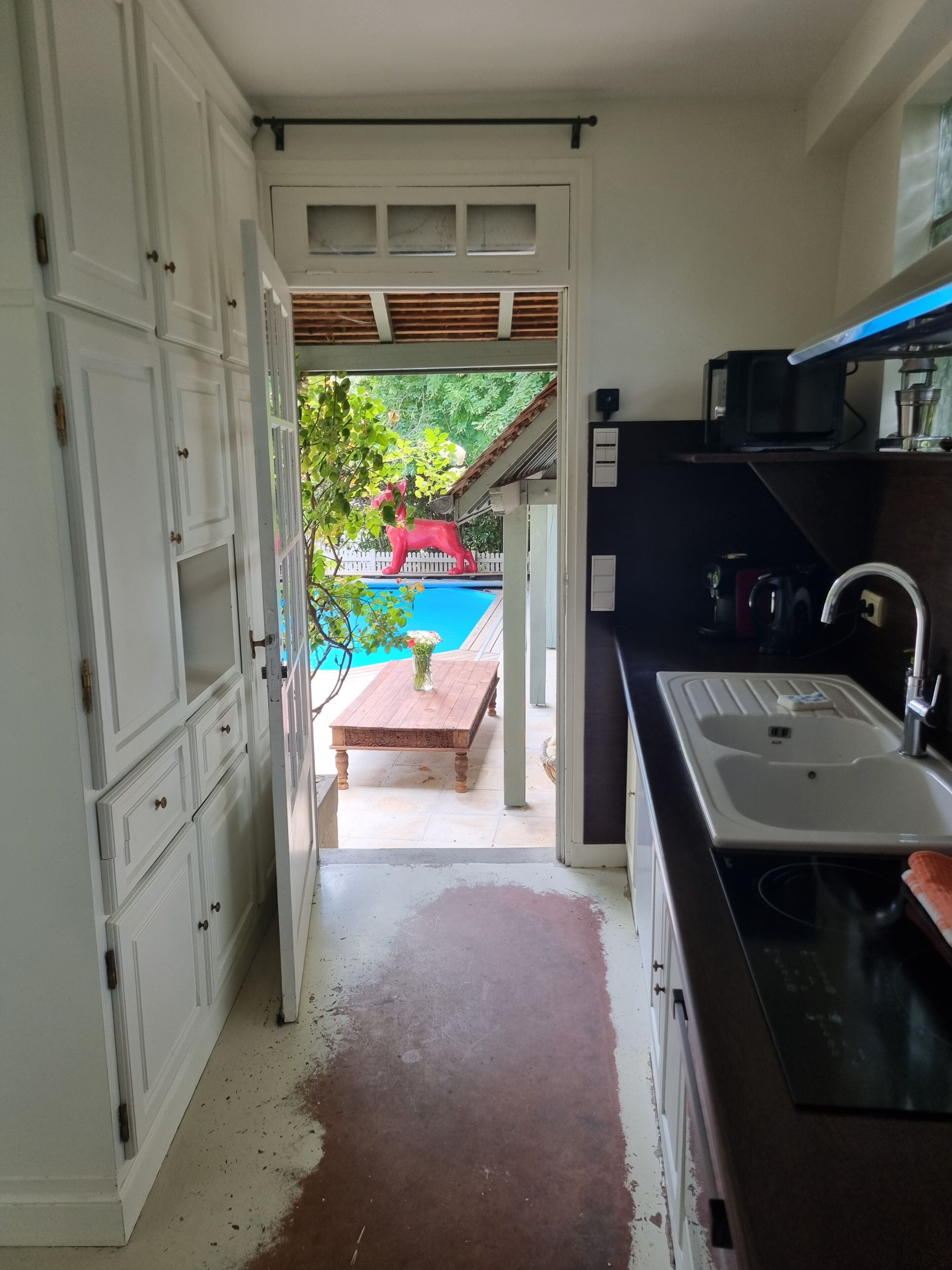 A kitchen with white cabinets, a sink, and a view of a pool and patio area.