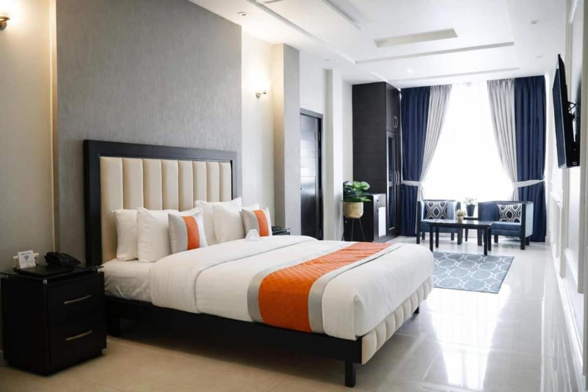 Une chambre d’hôtel avec un grand lit, des tables de chevet, un bureau avec des chaises et une vue sur l’extérieur par la fenêtre.