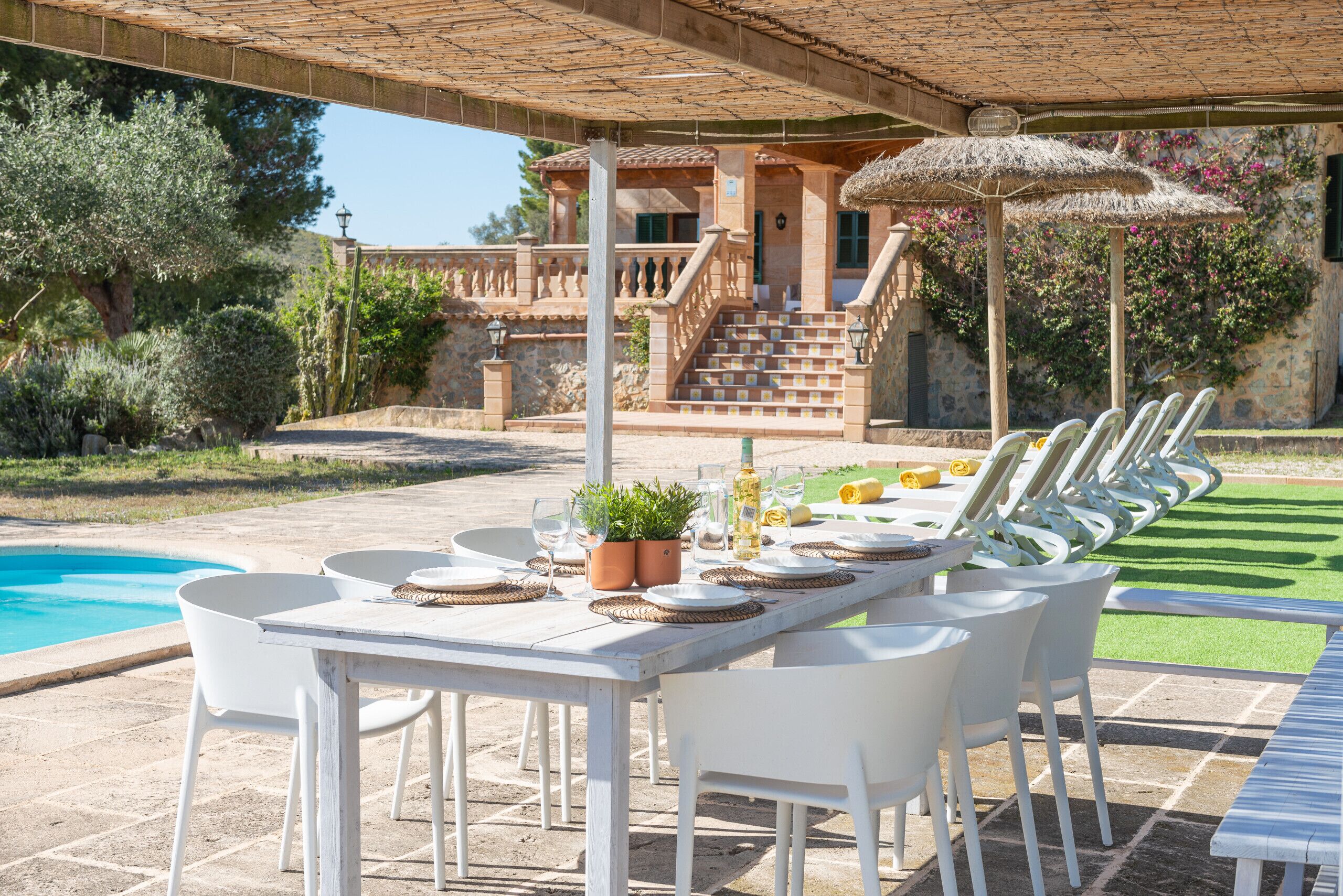 An outdoor dining area with a pool, white chairs, and a table set for a meal.