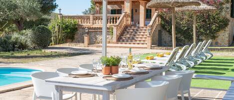 An outdoor dining area with a pool, white chairs, and a table set for a meal.