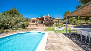 Una piscina amb zona de solàrium enrajolada, cadiretes i un porxo cobert.