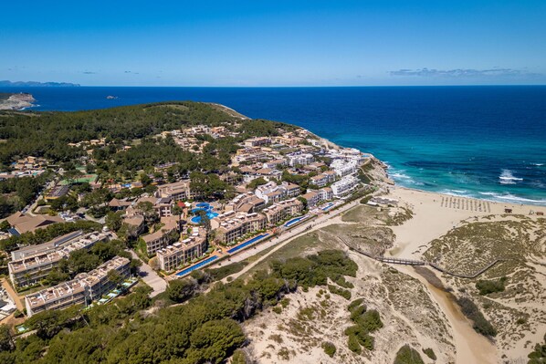 An aerial view of a coastal resort with multiple buildings, a beach, and a clear view of the ocean.
