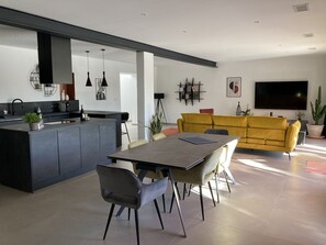 A modern kitchen with a central island, a dining area with a table and chairs, and a living area with a sofa and a TV.