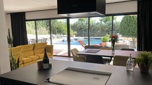 Eine moderne Küche mit einer großen Kochinsel, einem Essbereich mit Tisch und Stühlen sowie Blick auf einen Swimmingpool und Sitzgelegenheiten im Freien.