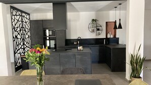 Eine moderne Küche mit dunklen Schränken, einer zentralen Kochinsel und einem Essbereich mit Tisch und Stühlen.