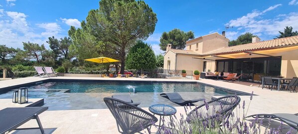 A swimming pool with lounge chairs and a yellow umbrella, surrounded by trees and a building with a tiled roof.