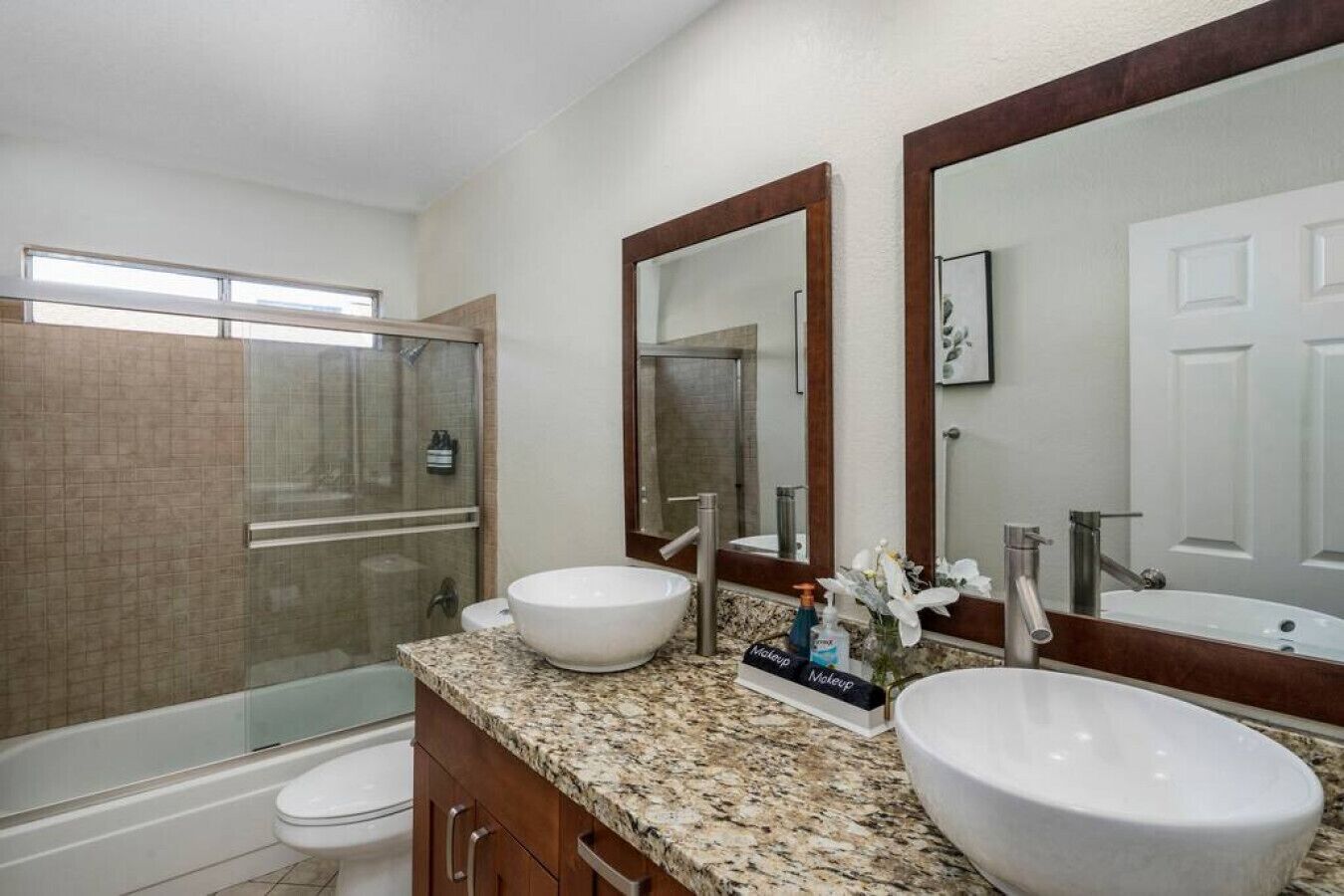 A bathroom with a shower, two sinks, a toilet, and a vanity with a mirror.