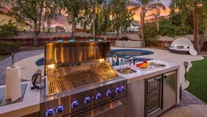 Una cocina exterior con una parrilla, un lavamanos y un horno empotrado.