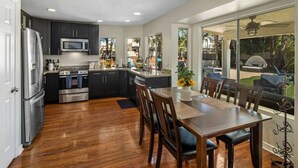 Una cocina moderna con armarios oscuros, electrodomésticos de acero inoxidable y una zona de comedor con un amplio ventanal con vistas a un jardín.