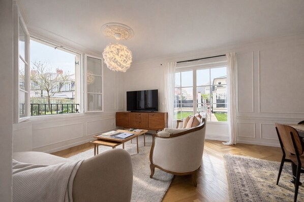 Un salon spacieux doté d’une grande fenêtre, d’un téléviseur à écran plat, d’un meuble en bois, d’un canapé et d’une table à manger.