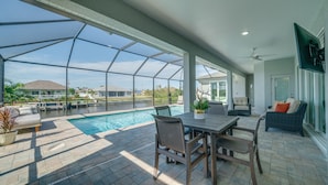 Un espace extérieur abrité comprenant une piscine, des sièges et une vue sur une maison située de l’autre côté d’une étendue d’eau.