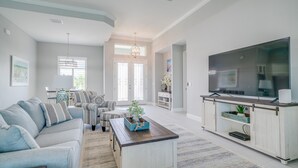 Un salon spacieux doté d’un grand téléviseur à écran plat, d’un ensemble de canapés, d’une table basse et d’un meuble TV avec espace de rangement.