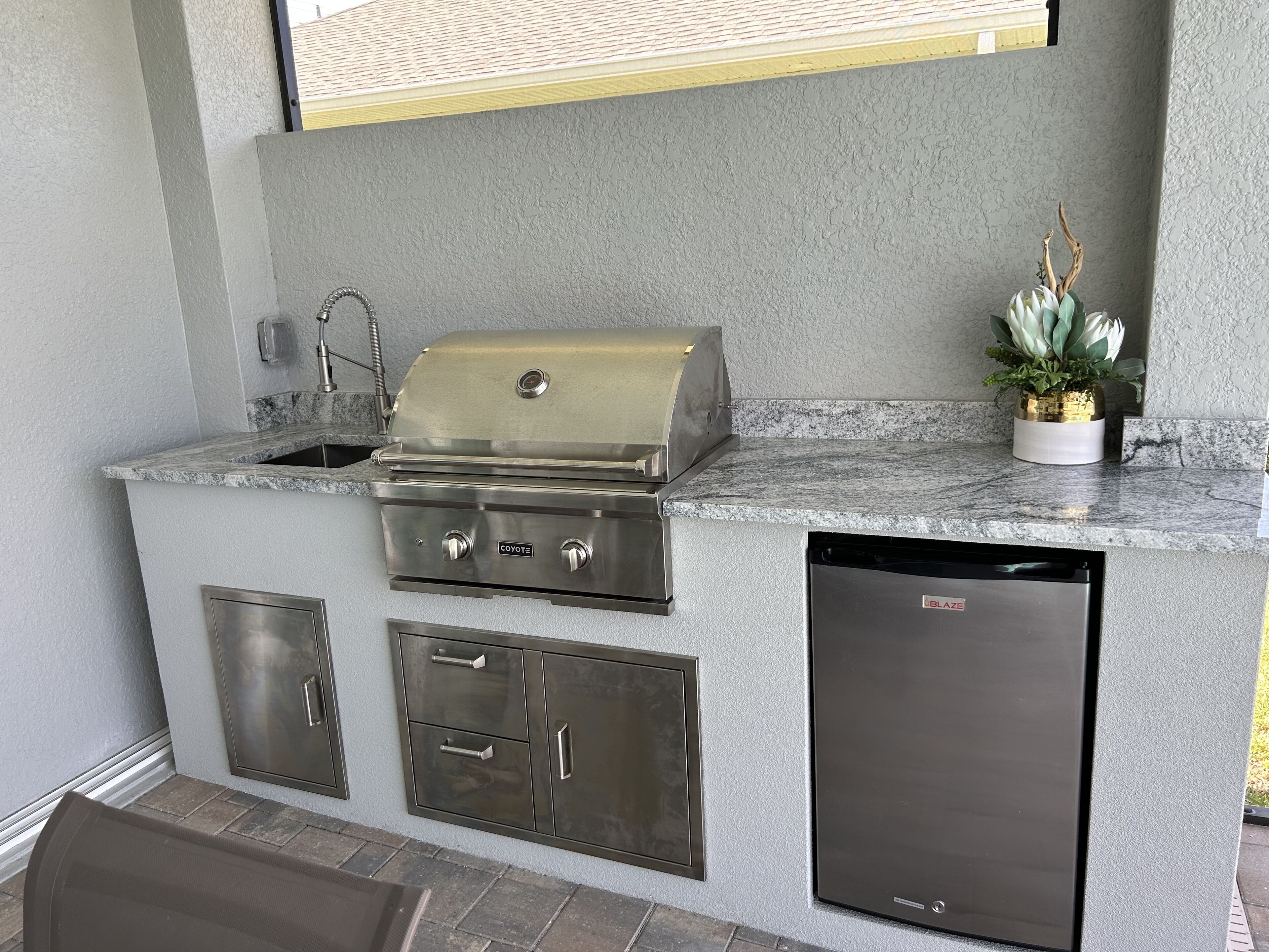An outdoor kitchen with a built-in grill, a sink, and a dishwasher.