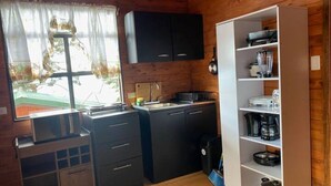 Kompakti keittiö, jossa on puiset kaapit, pesuallas ja sisäänrakennettu valkoinen hyllykkö.