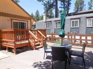 Une terrasse en bois avec une table et des chaises, un parasol et, au fond, un bâtiment doté de fenêtres et d’une cheminée.