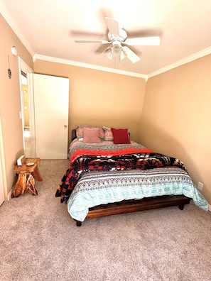 A bedroom with a bed, a ceiling fan, a wooden stool, and a door.