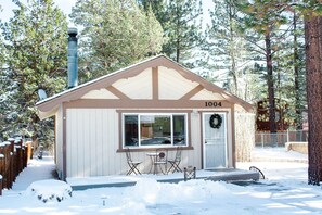 Une petite cabane portant le numéro 1004, avec une fenêtre, une porte décorée d’une guirlande et une petite table entourée de chaises à l’extérieur.