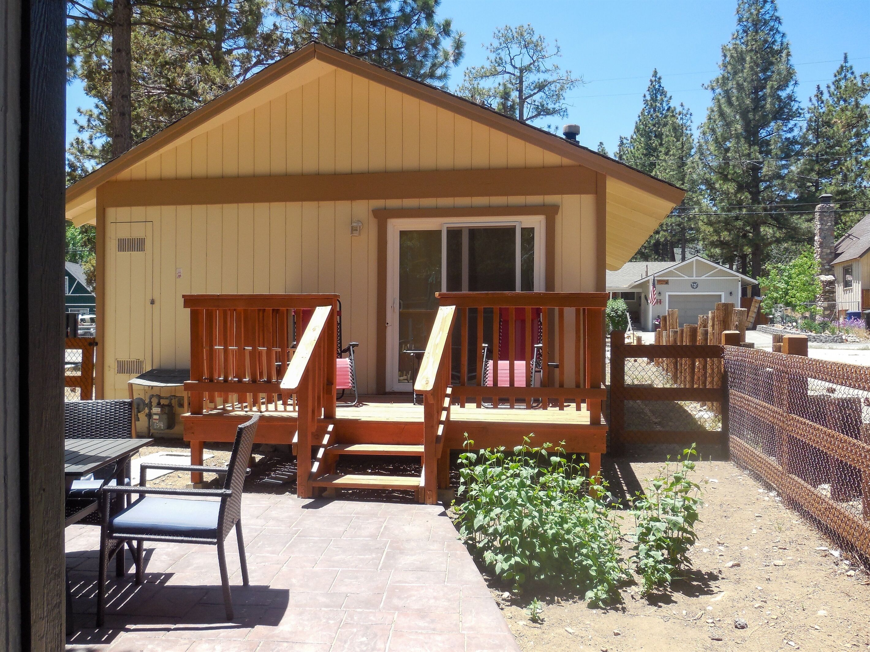 A wooden cabin with a porch, outdoor seating, and a fenced garden area.