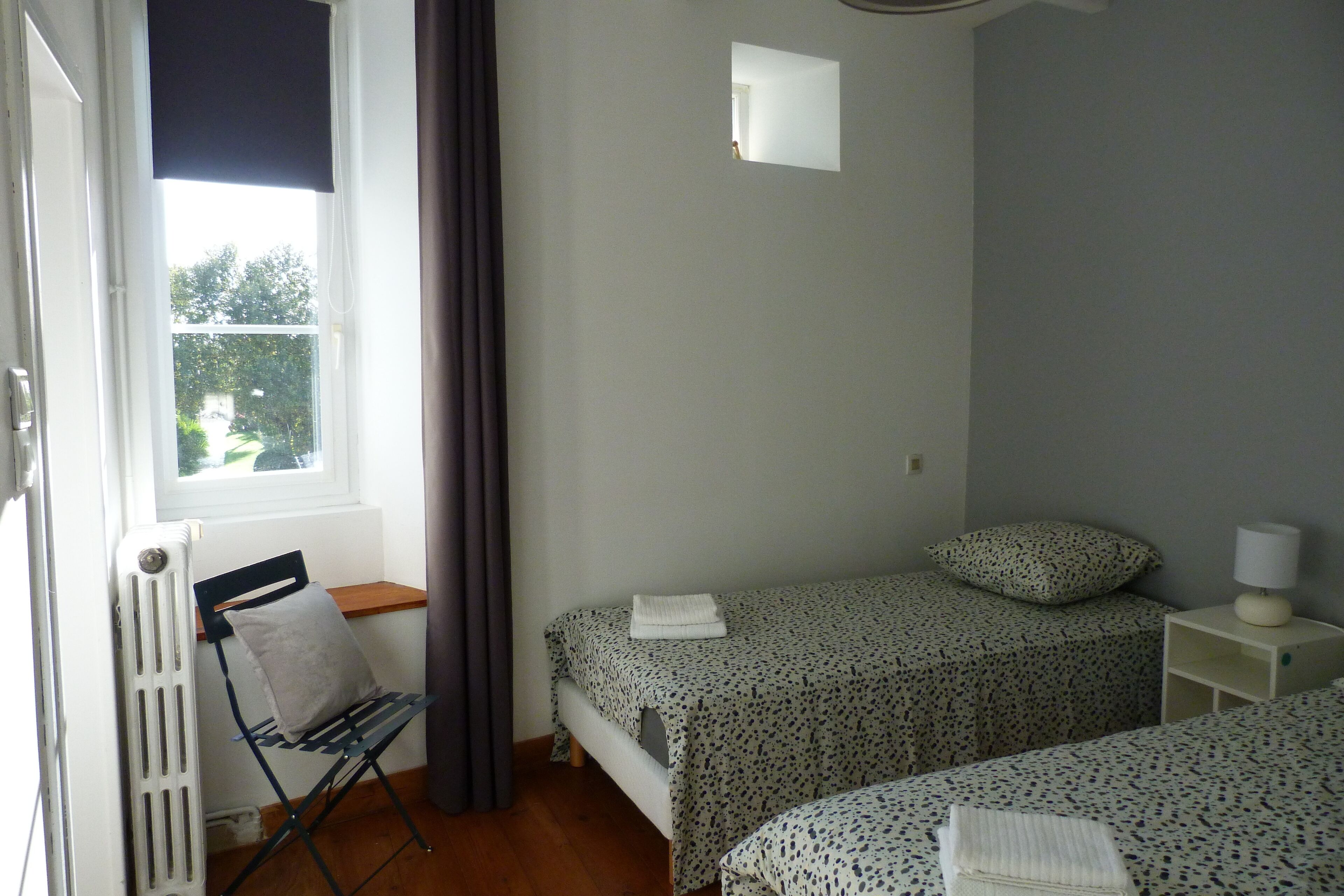 A small, simple room with two beds, a radiator, a window, and a chair.