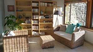 A cozy living room with a large bookshelf, wicker furniture, and a window with a view.