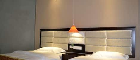 A hotel room with two beds, a headboard with a light fixture, and a nightstand with a lamp.