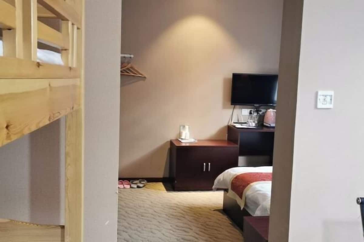 A hotel room with a bunk bed, a small desk with a TV, a wardrobe, and a bedside table.