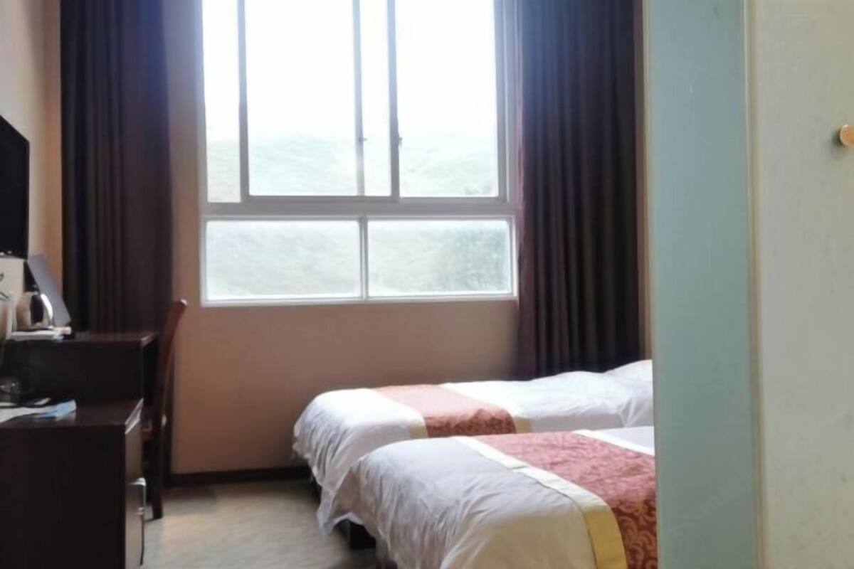 A hotel room with two beds, a desk, a chair, and a window with curtains.