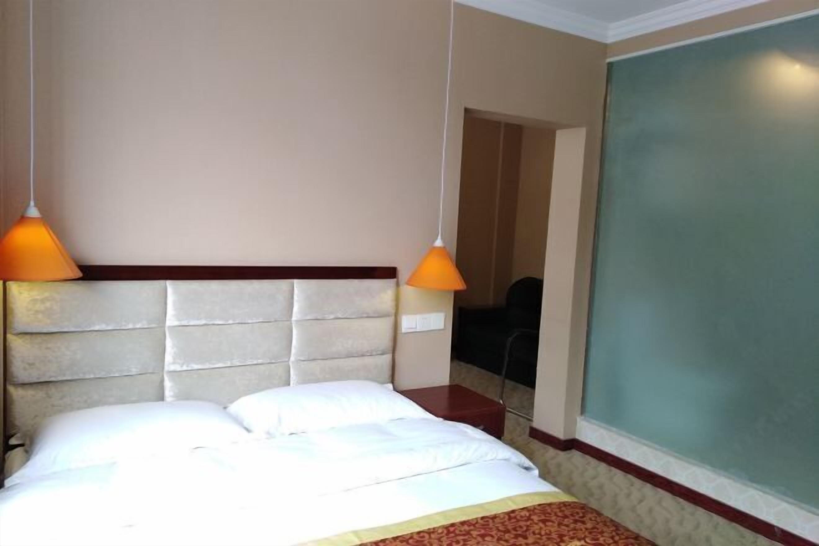 Una habitación de hotel con una cama, dos lámparas colgantes anaranjadas, un cabecero, una ventana con vistas y una puerta que da a otra habitación.