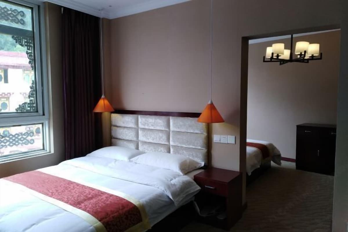Une chambre d’hôtel avec un lit, une table de chevet, une lampe, une armoire et une fenêtre avec des rideaux.