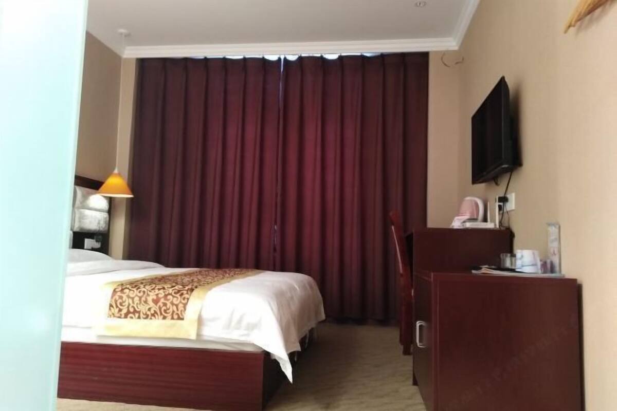 A hotel room with a bed, a desk, a television, and a window with curtains.