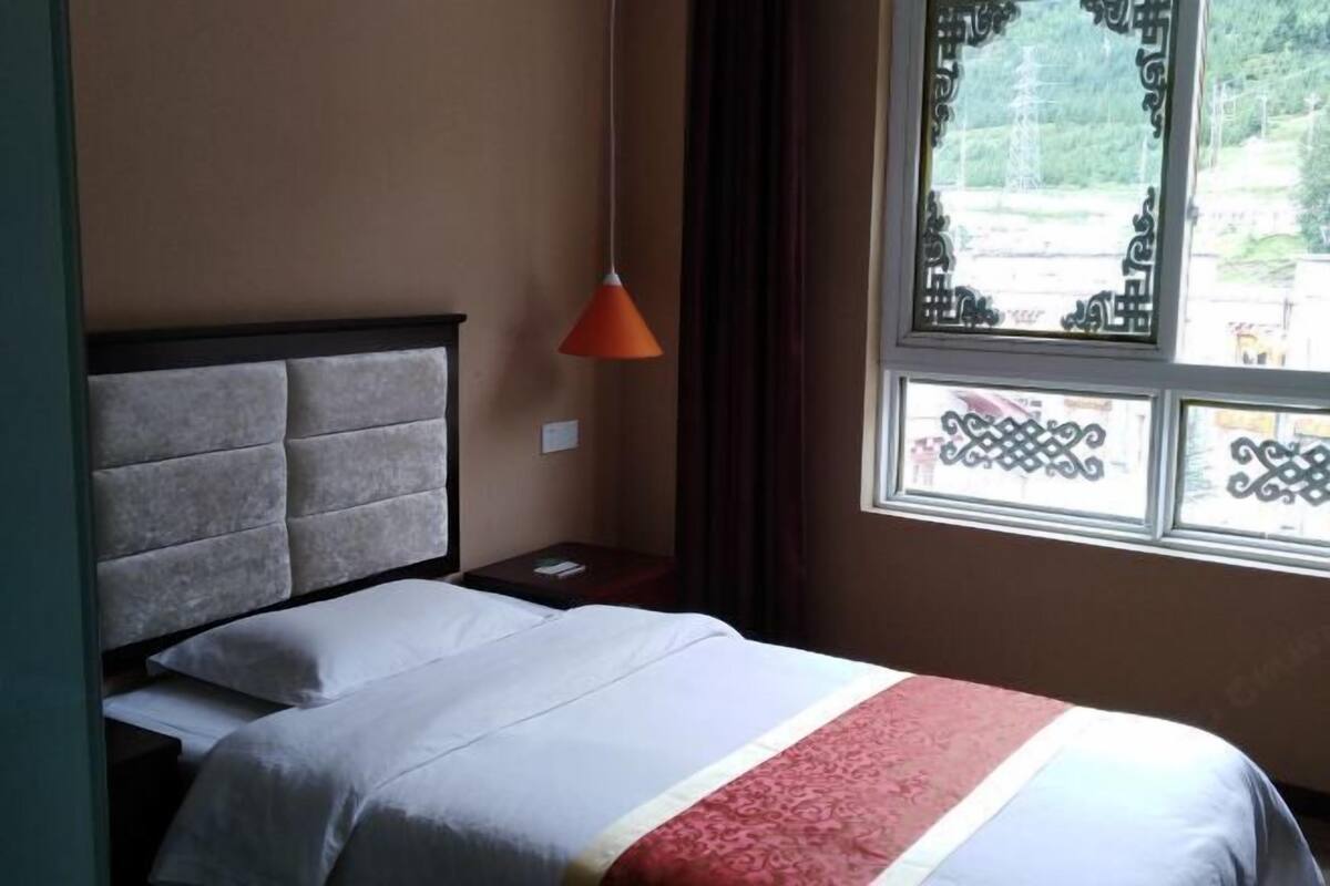 A hotel room with a bed, a nightstand, a red lamp, and a window with decorative ironwork.