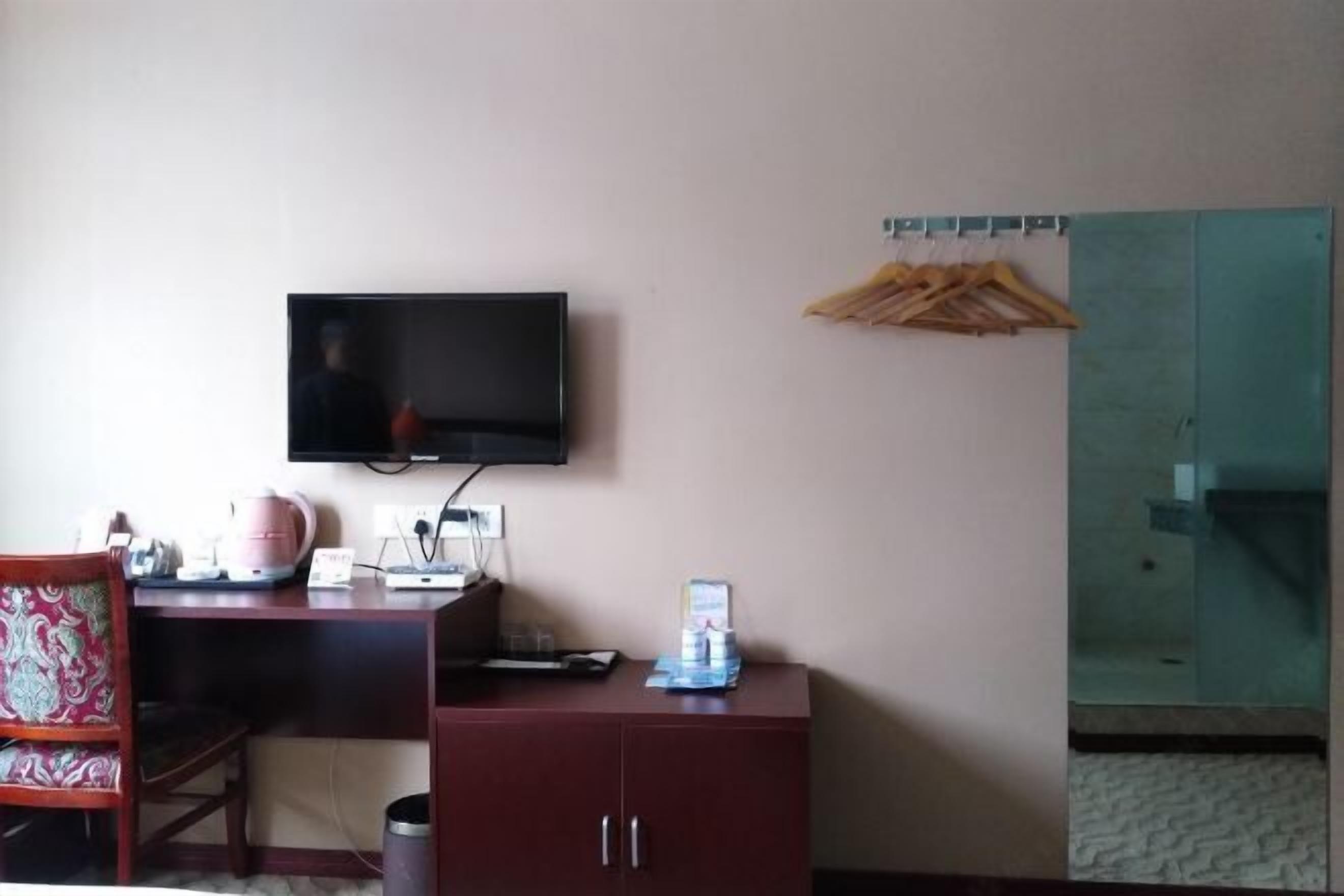 Ein Hotelzimmer mit Schreibtisch, Wandfernseher, Schrank und Spiegel.