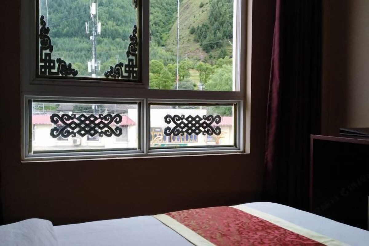 Une chambre d’hôtel avec un lit, une fenêtre ornée de grilles en fer décoratives et une vue sur un paysage verdoyant.