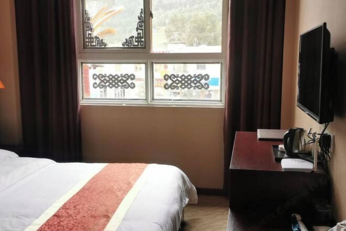A hotel room with a bed, a desk with a computer, a TV, and a window with decorative ironwork.