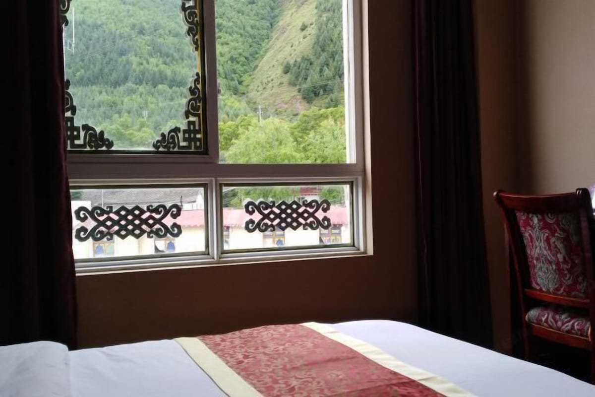 Une chambre avec un lit, une fenêtre ornée de grilles en fer décoratives et une vue sur un paysage verdoyant.